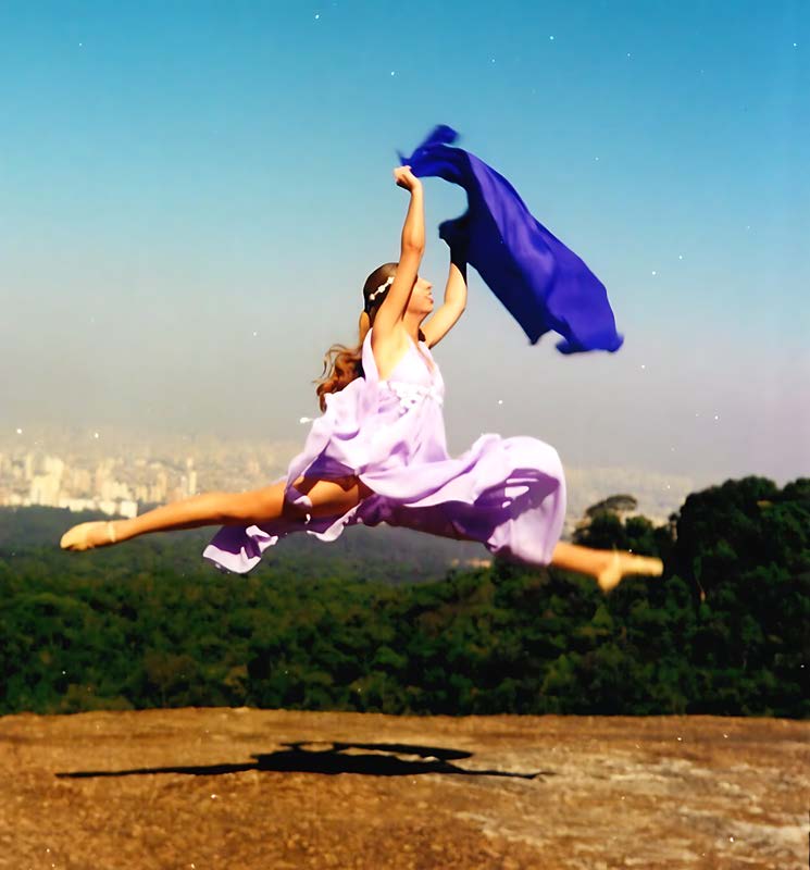 Bailarina saltando ao ar livre com pernas em escala segurando um tecido azul