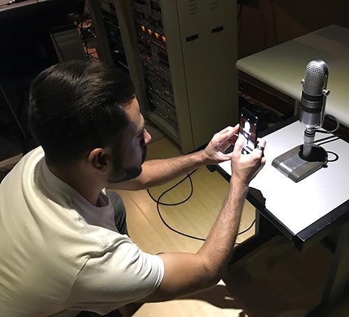 Homem mexendo no celular com um microfone à sua frente